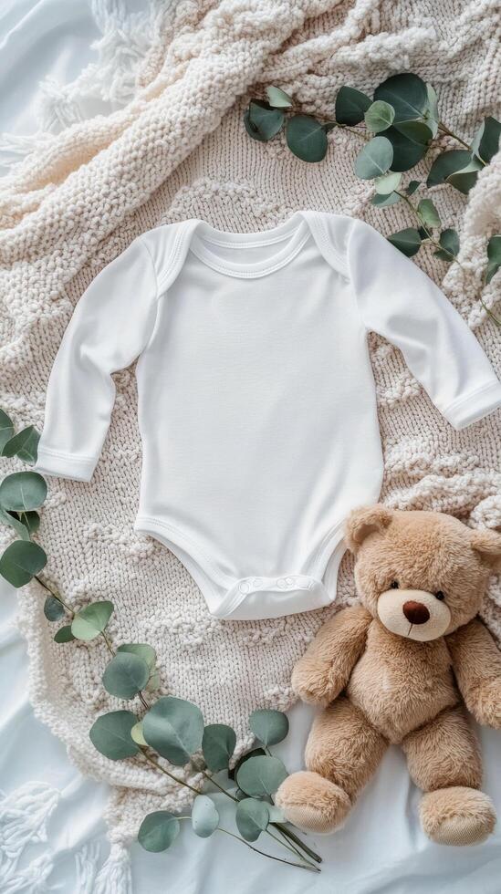 Soft baby onesie arranged with greenery and a bear on a cozy blanket photo