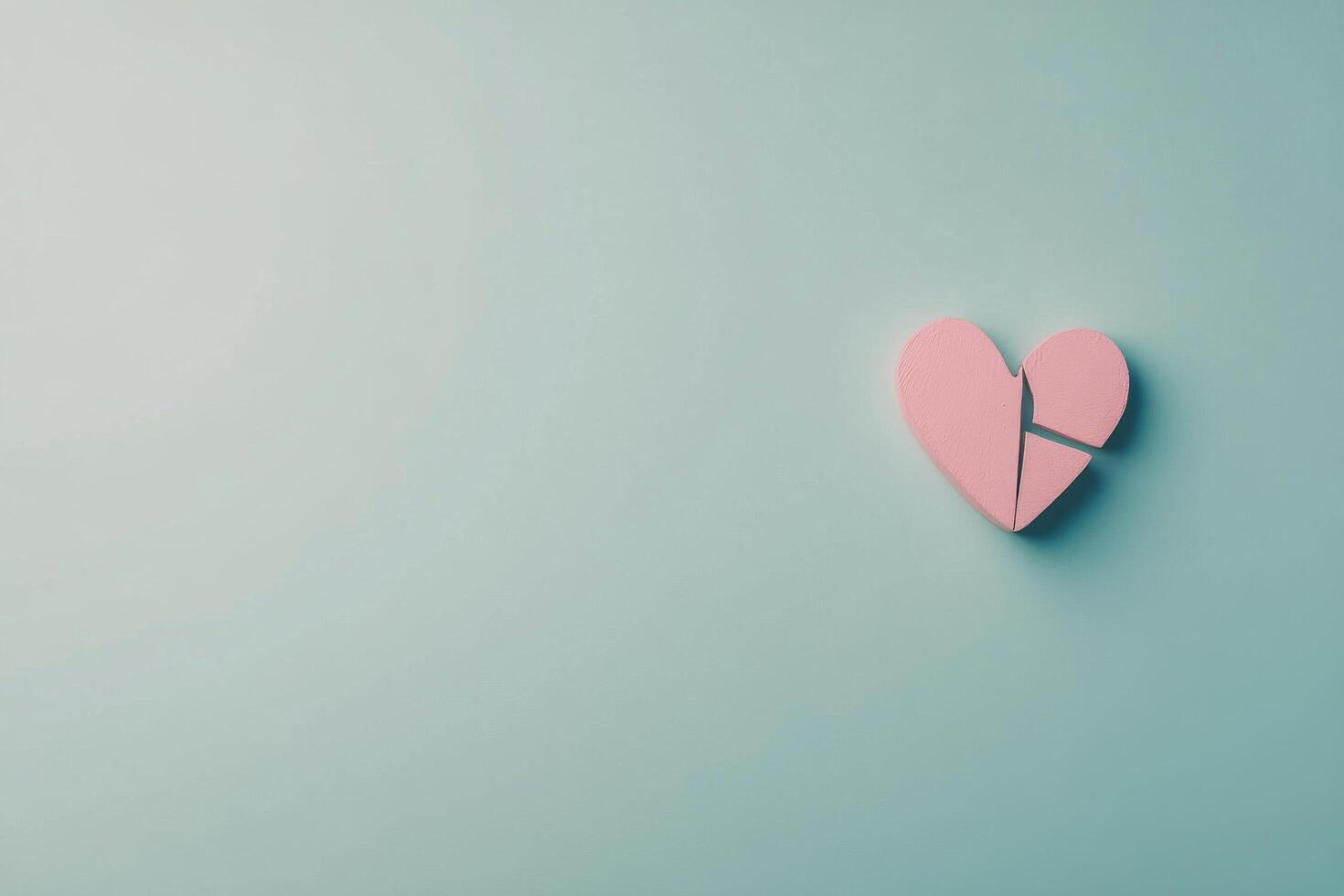 Pink heart shaped piece broken on a light blue background representing love and relationships photo