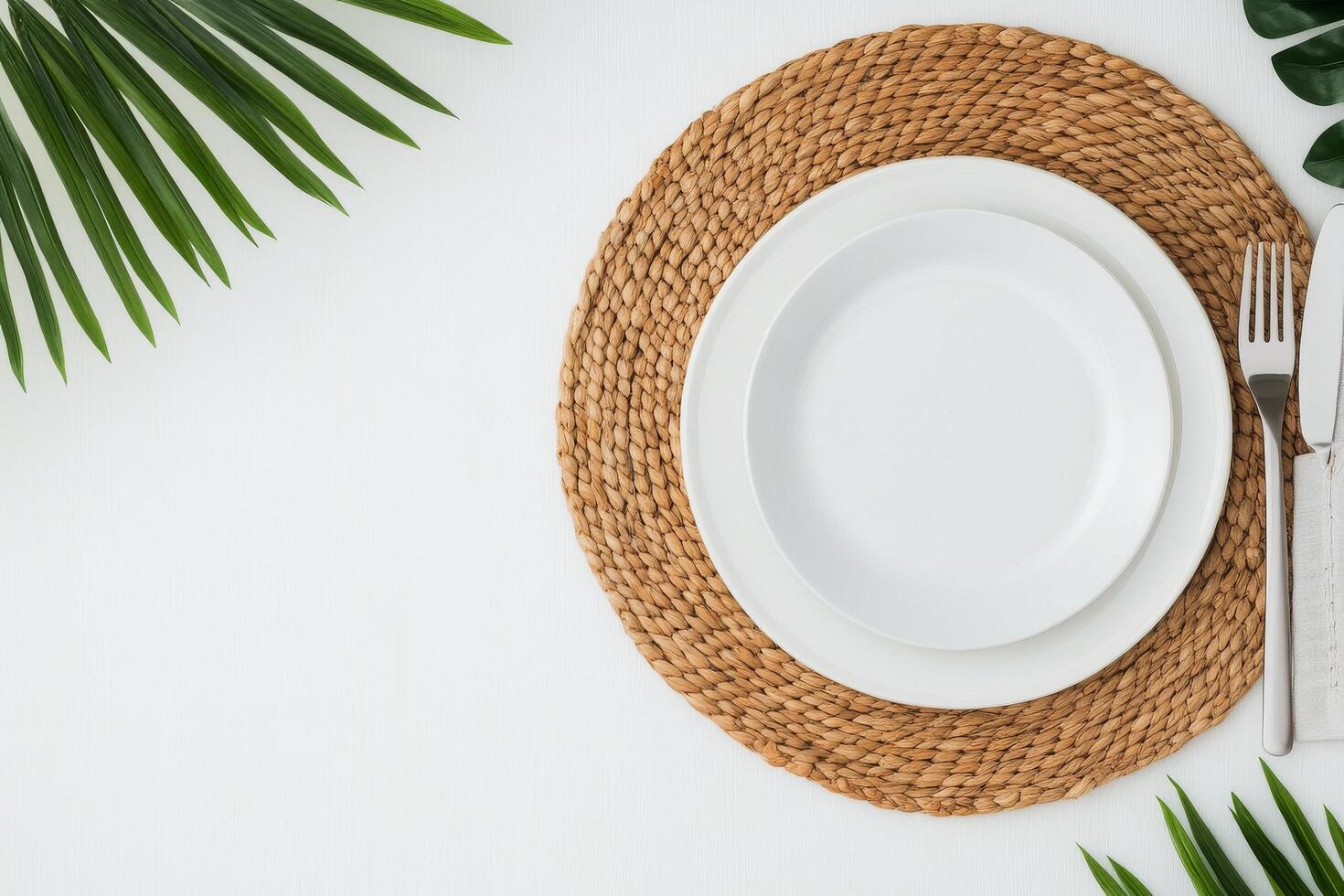 Clean white plate on a woven placemat surrounded by green foliage and cutlery photo