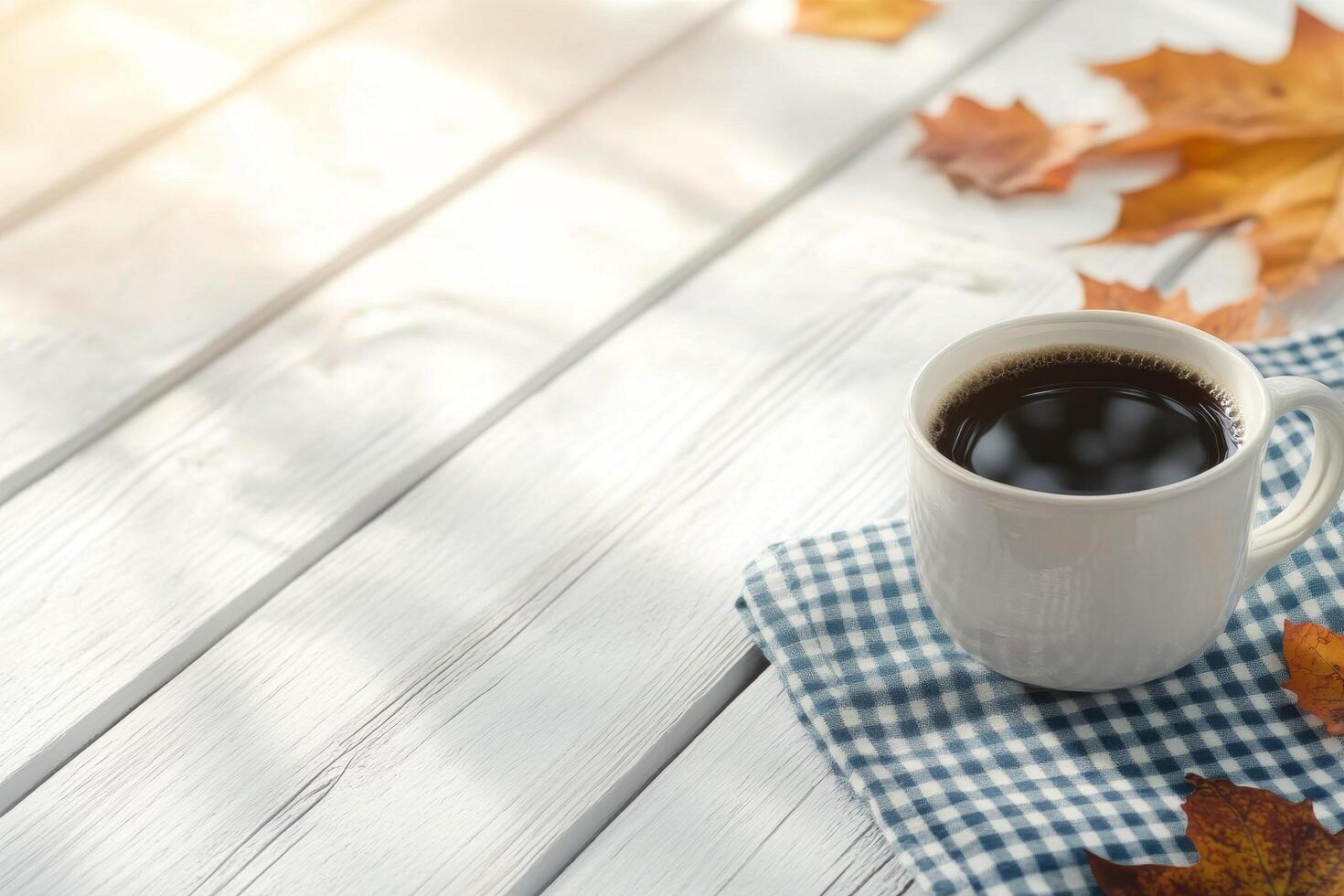 Warm coffee cup resting on a checkered napkin surrounded by autumn leaves photo