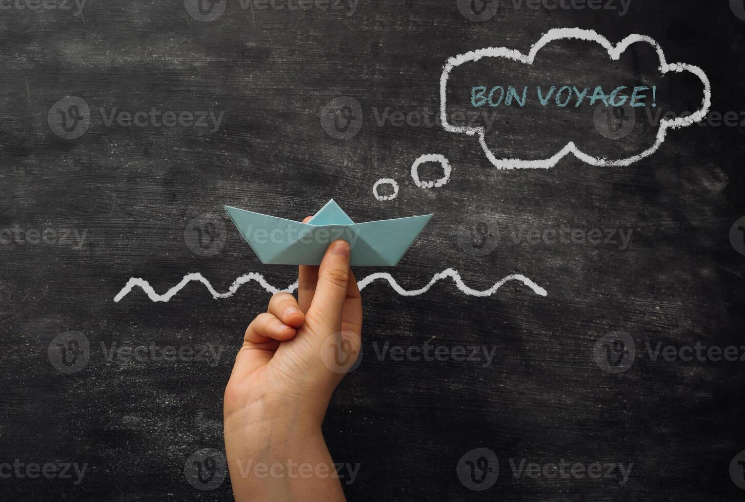 A hand holding a paper boat in a chalkboard with the words Bon Voyage photo