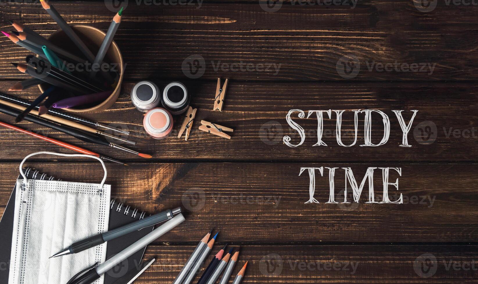 A wooden table with a bowl of pencils, a bottle, and a pair of scissors photo