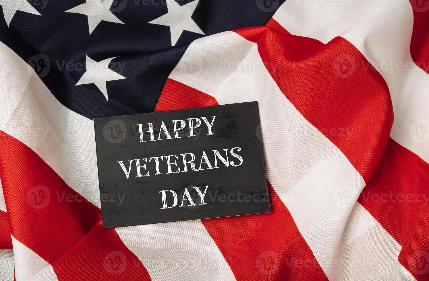 Black sign with the words Happy Veterans Day is placed on top of a red photo