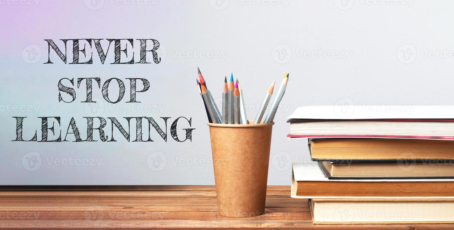 Never stop learning. A pencil holder with pencils sits on a table with a stack of books photo