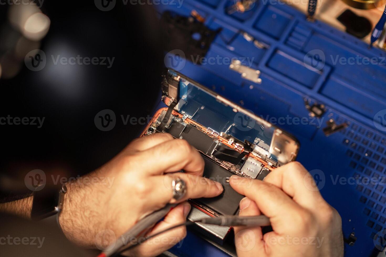 Technician performing smartphone battery repair in a workshop with tools and components while focused on detail photo