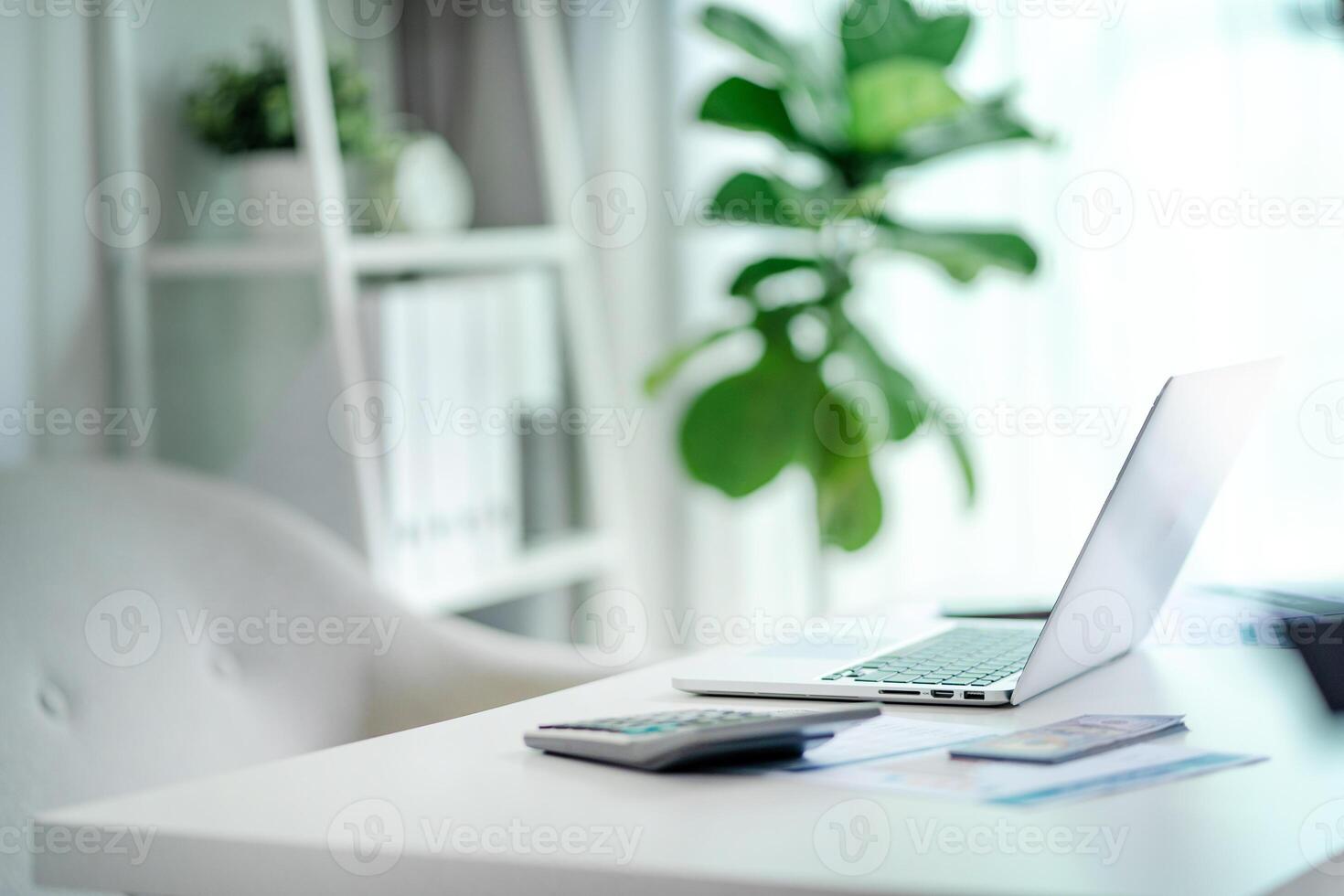 A white desk with a laptop, calculator, and a potted plant. The desk is clean and organized, with a sense of productivity and focus. The potted plant adds a touch of nature and freshness to the space photo