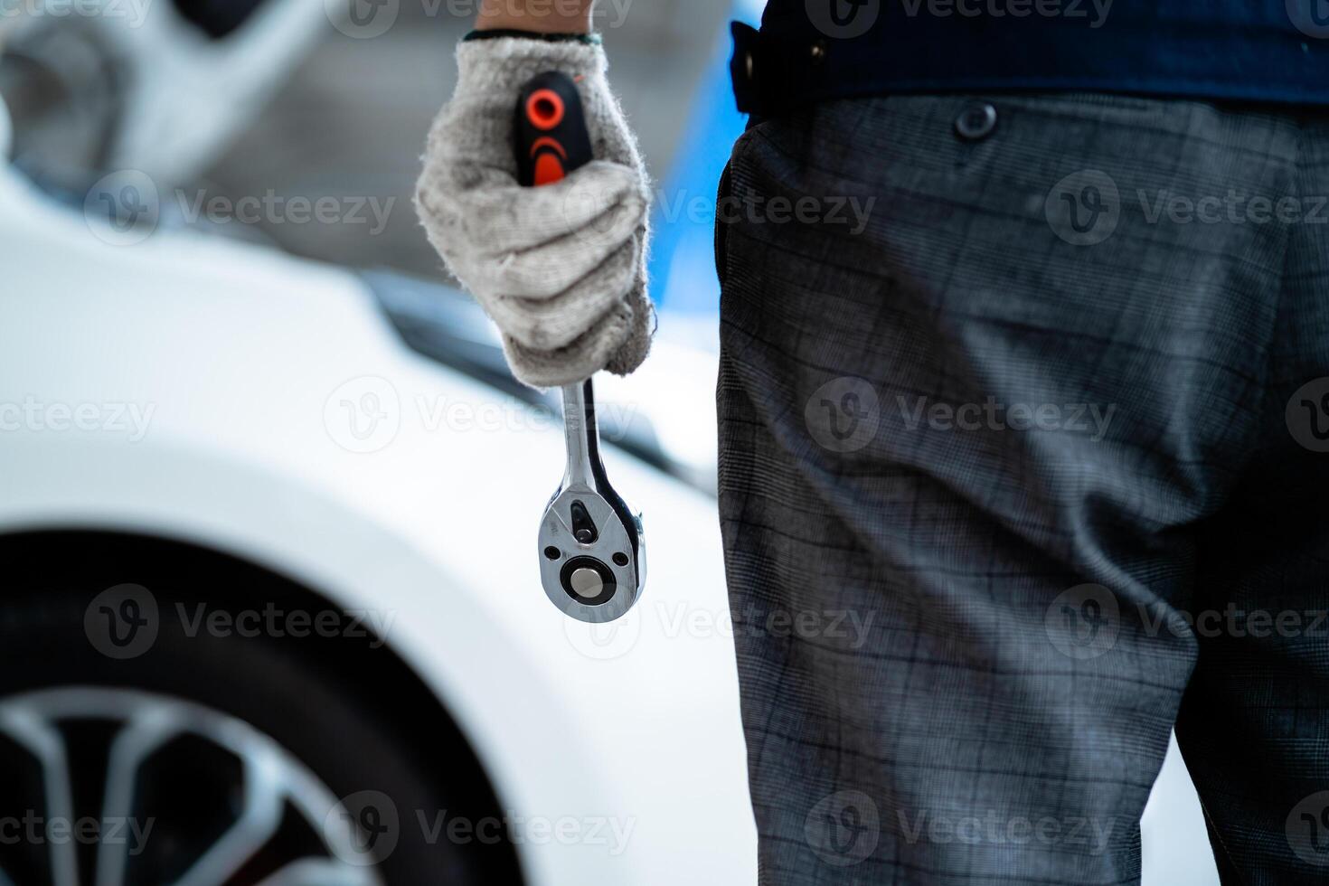 A man is holding a wrench and wearing gloves. He is standing next to a car. Concept of work and maintenance, as the man is likely a mechanic or a car enthusiast photo