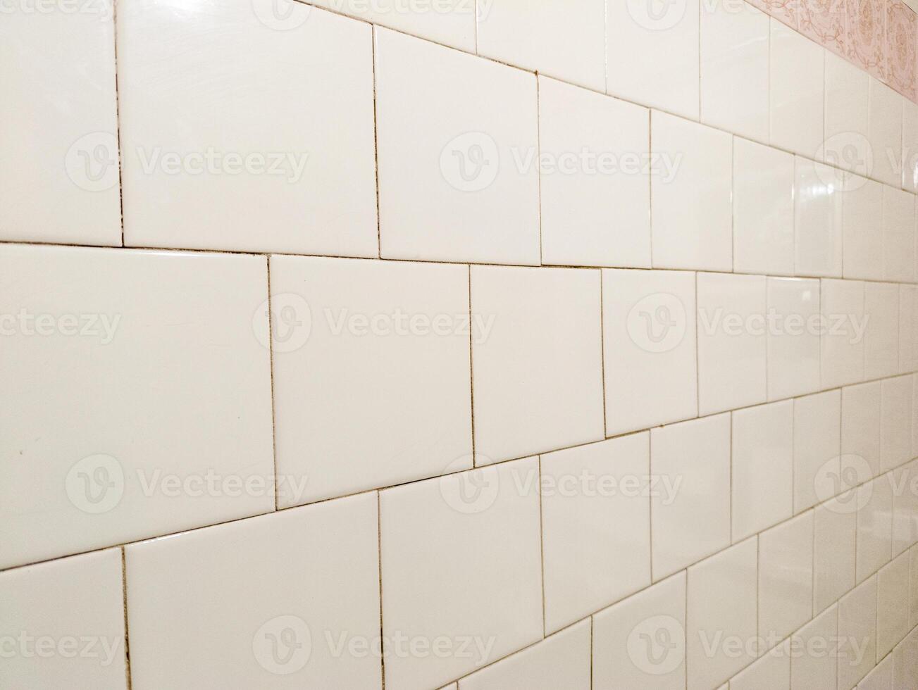 A white tiled wall in a bathroom with a pink and white tile border photo