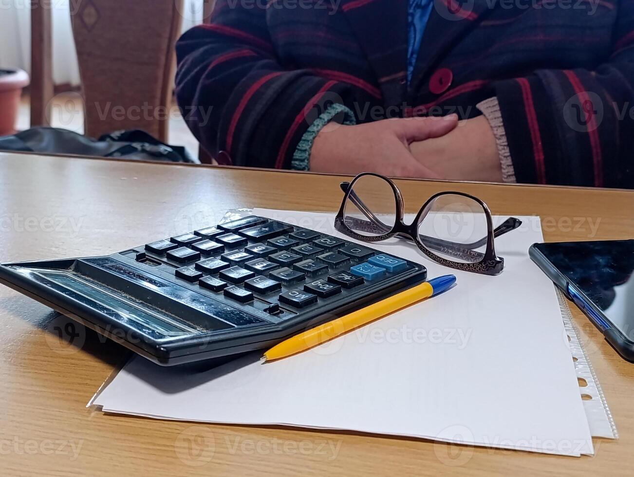 A person sitting at a table with a calculator pen and glasses photo