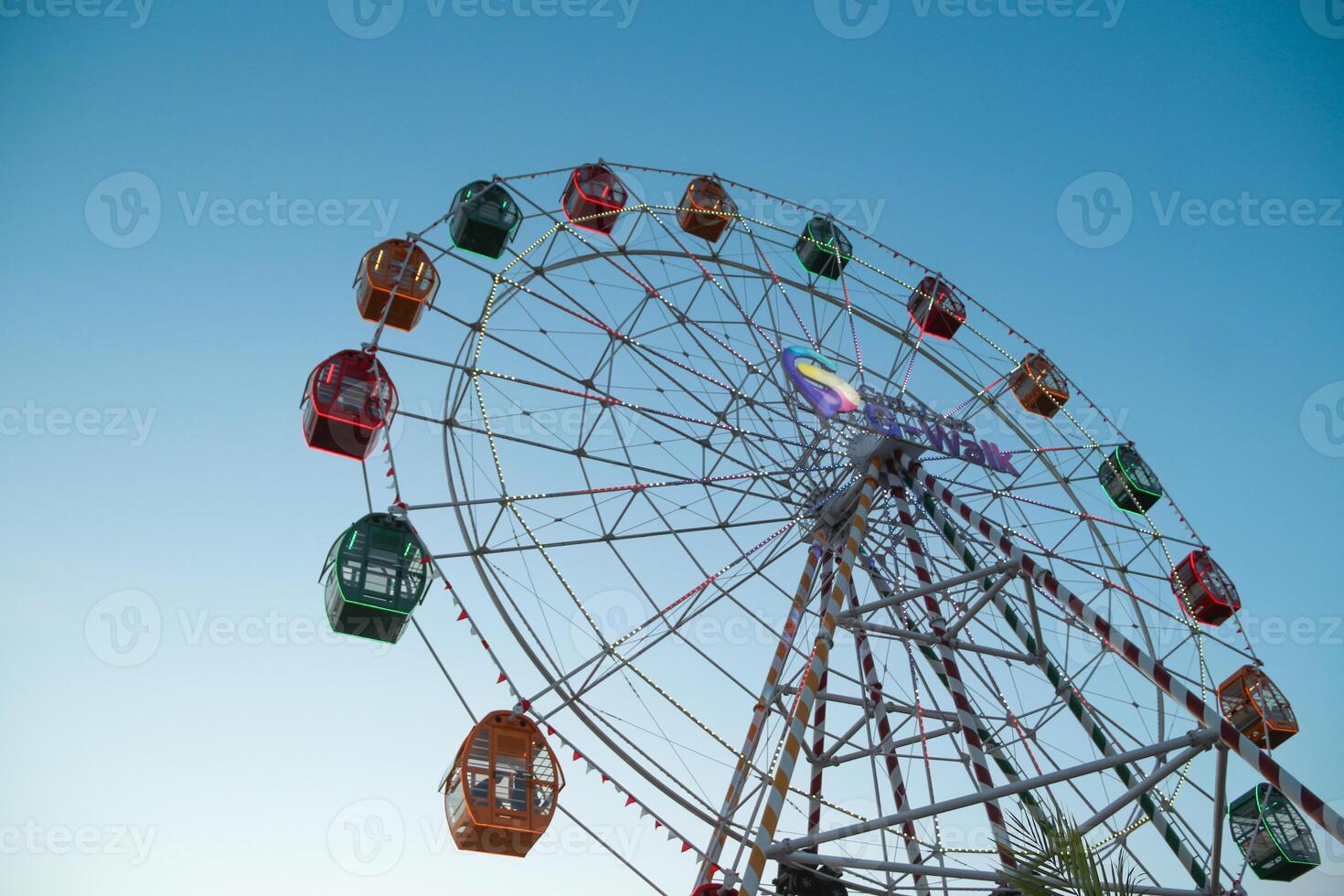 From below static ferris wheel against a clear blue sky, showcasing its symmetry and colorful patterns on the passenger cabins photo