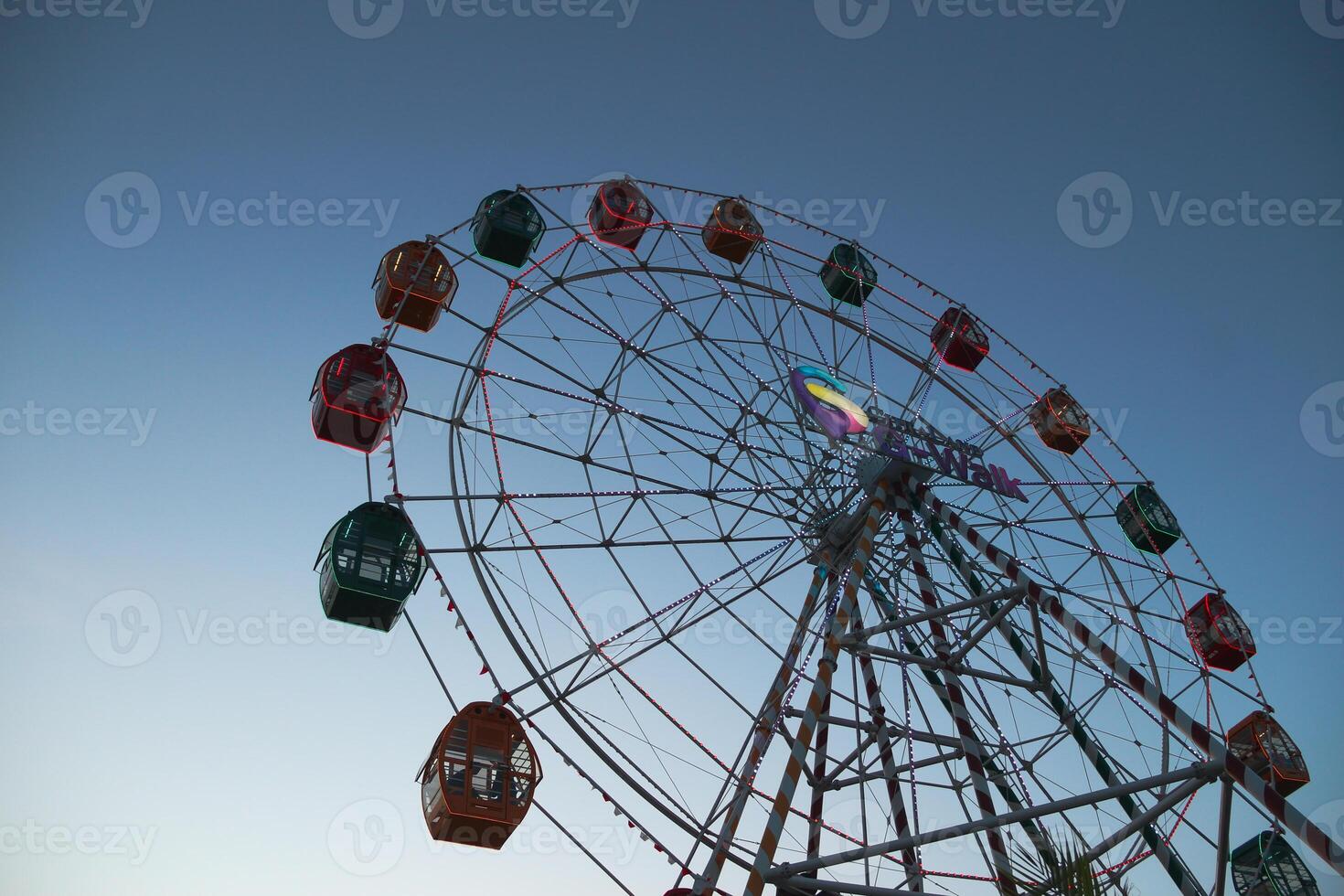 From below static ferris wheel against a clear blue sky, showcasing its symmetry and colorful patterns on the passenger cabins photo
