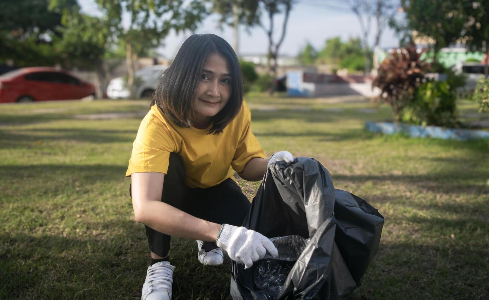 Asian woman picking plastic bottle into trash plastic bag black clean up ecology environmental ecology concepts, looking at the camera and smiling photo