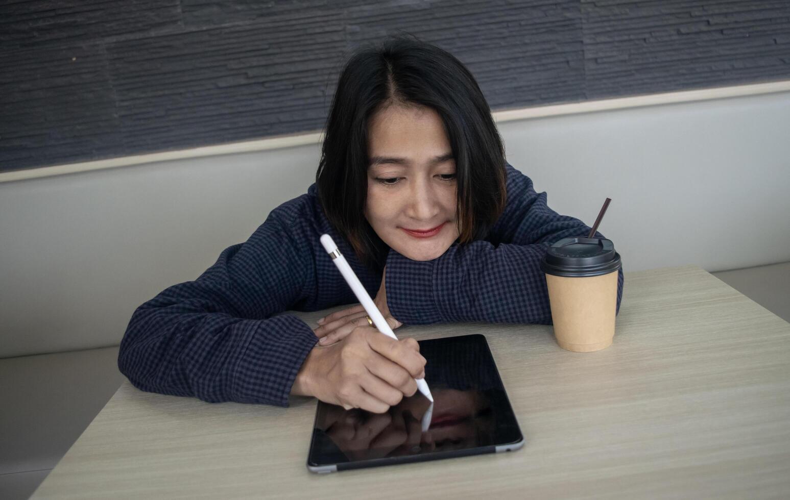 Asian woman sitting at cafe holding stylus pen writing on tablet relaxing on vacations, lifestyles concepts photo