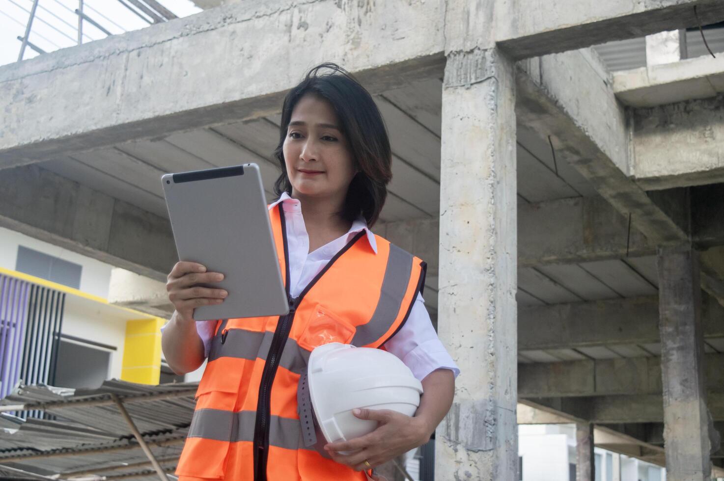 Engineer civil woman wearing uniform safety and holding hardhat using tablet working inspector new project building at construction site photo