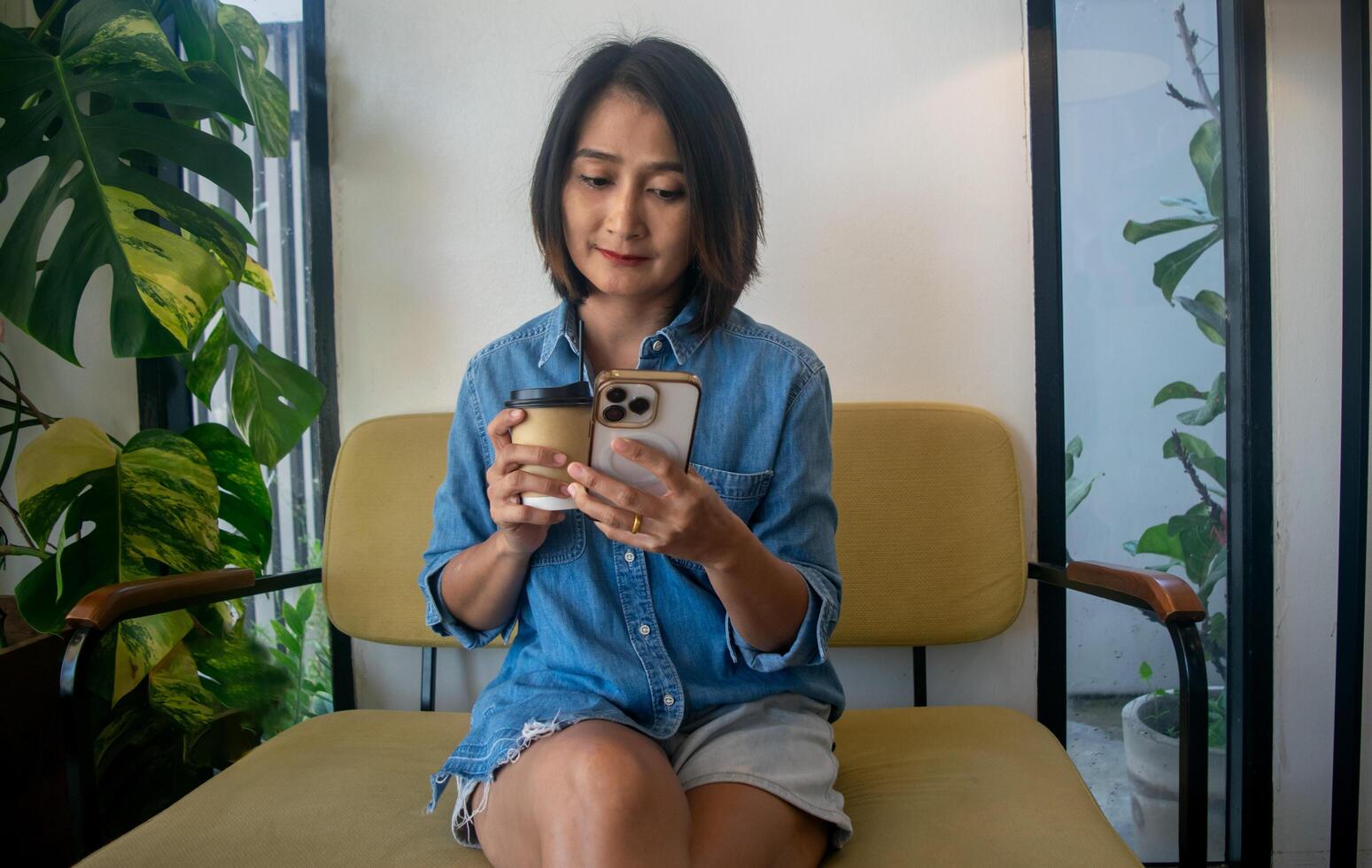 Asian woman sitting on sofa hand holding coffee cup and using mobile smart phone shopping online relaxing holiday concepts photo