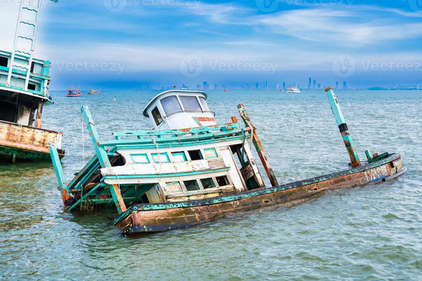 Wooden Fishing Vessel Wreckage Partially Submerged in Water with Skyline in the Distance at Chonburi, Thailand. photo