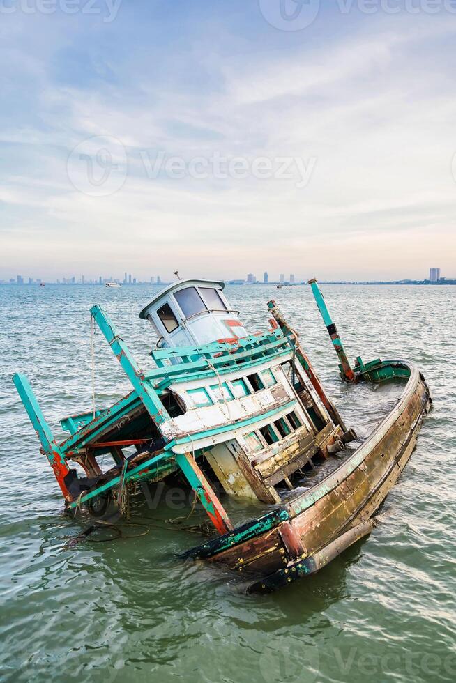Wooden Fishing Vessel Wreckage Partially Submerged in Water with Skyline in the Distance at Chonburi, Thailand. photo