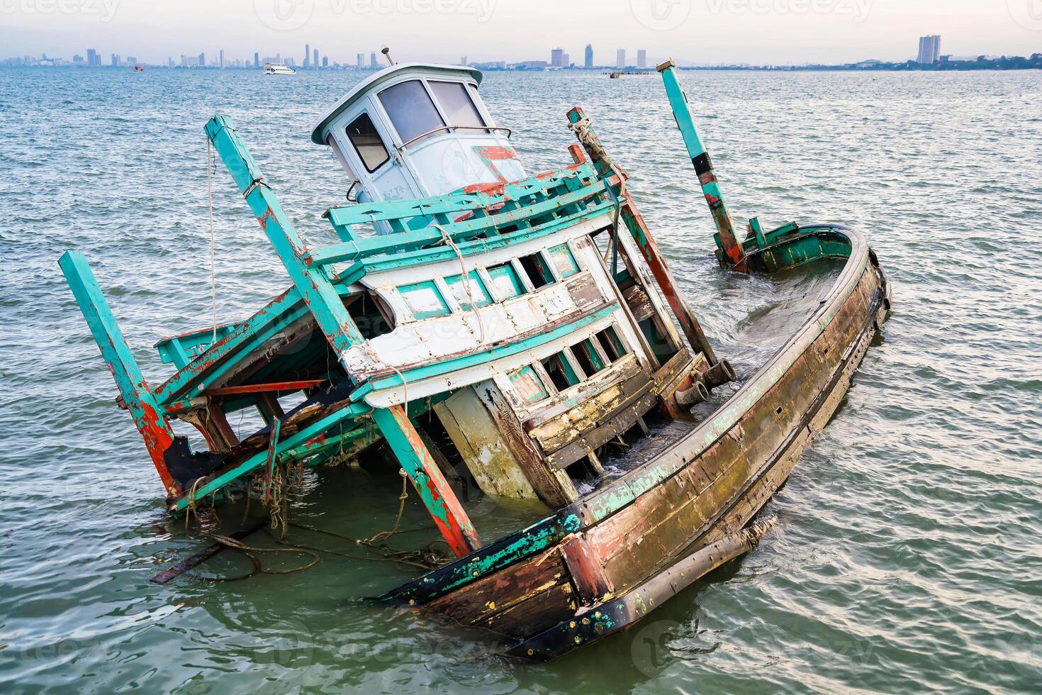 Wooden Fishing Vessel Wreckage Partially Submerged in Water with Skyline in the Distance at Chonburi, Thailand. photo