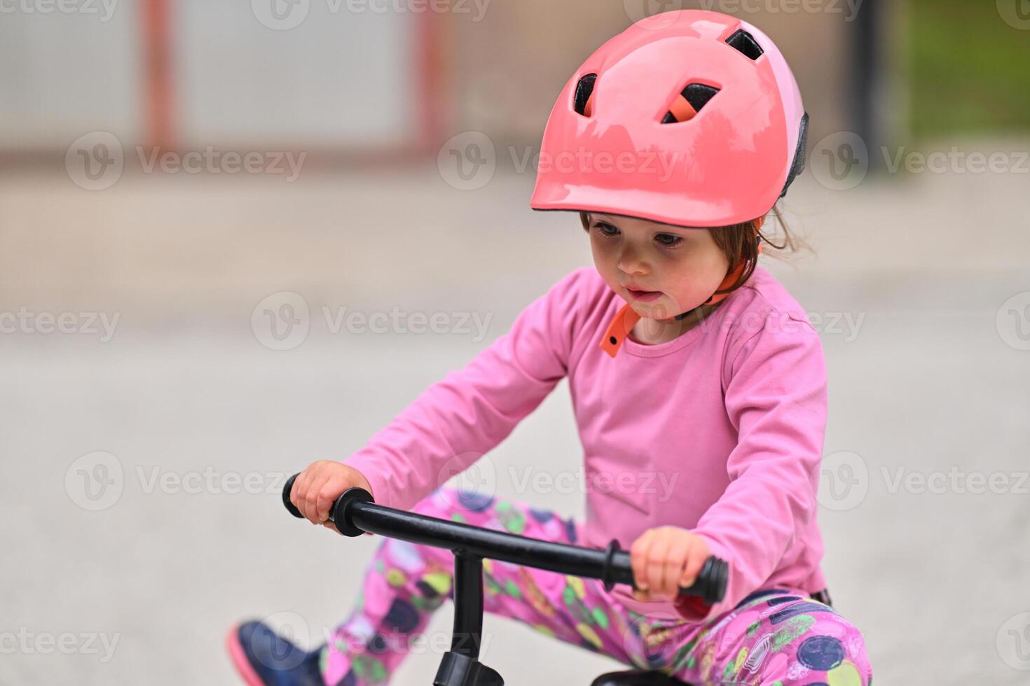 A little girl, dressed in a cute outfit and wearing a helmet, excitedly learning to ride her bike for the first time, filled with joy and determination. photo