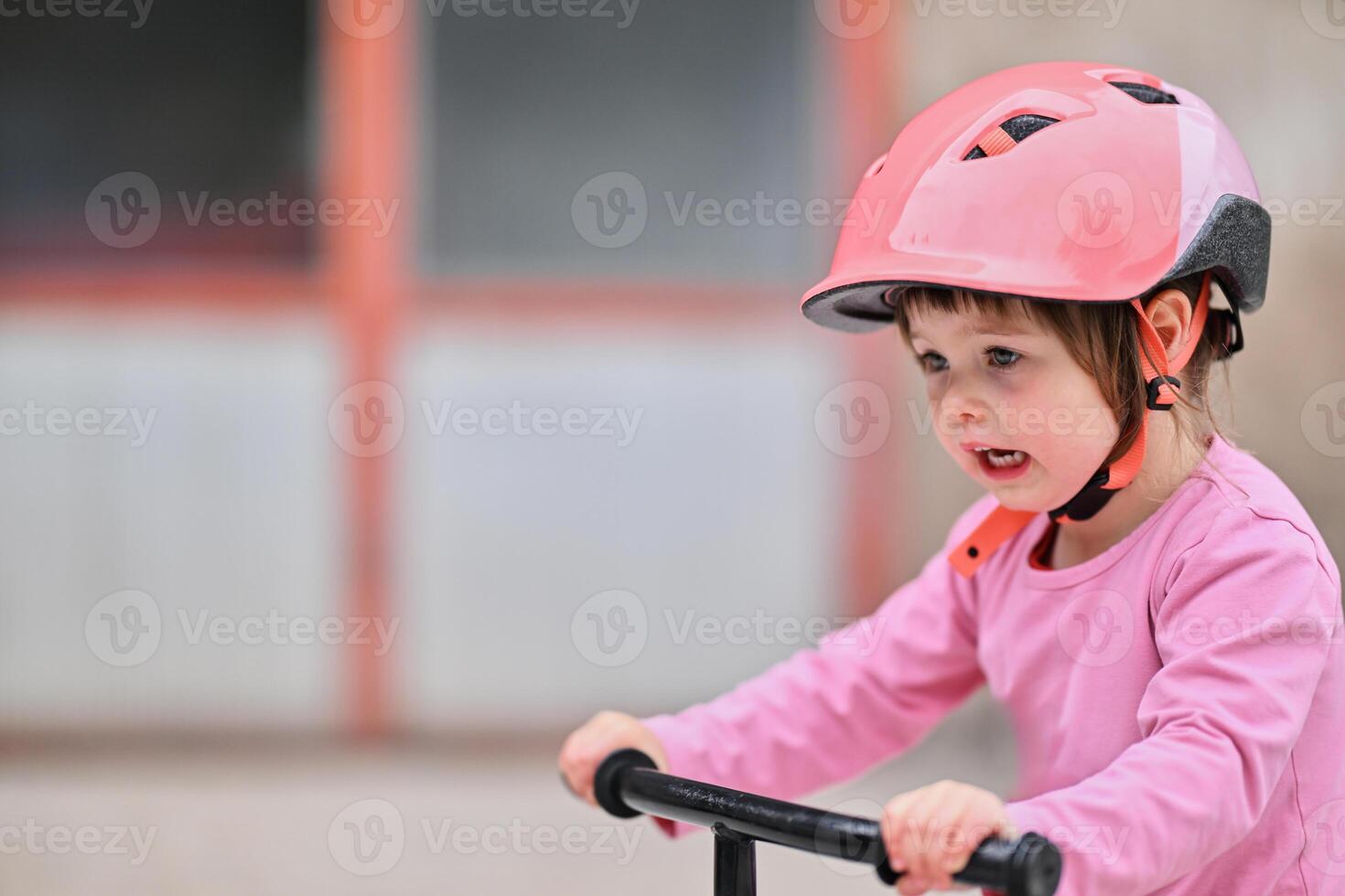 A little girl, dressed in a cute outfit and wearing a helmet, excitedly learning to ride her bike for the first time, filled with joy and determination. photo