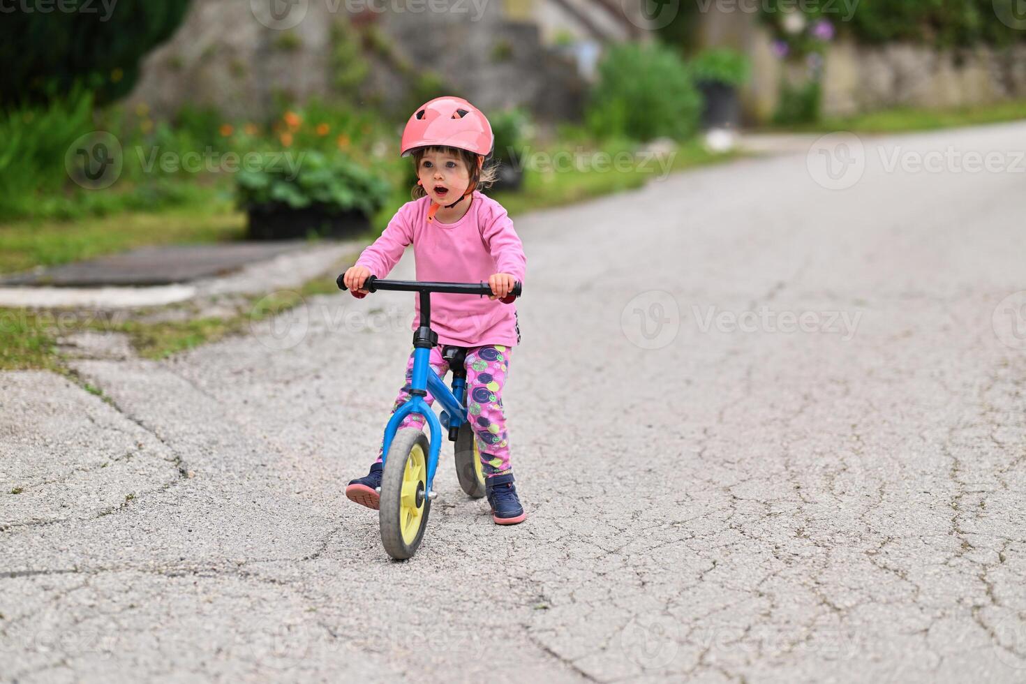 A little girl, dressed in a cute outfit and wearing a helmet, excitedly learning to ride her bike for the first time, filled with joy and determination. photo