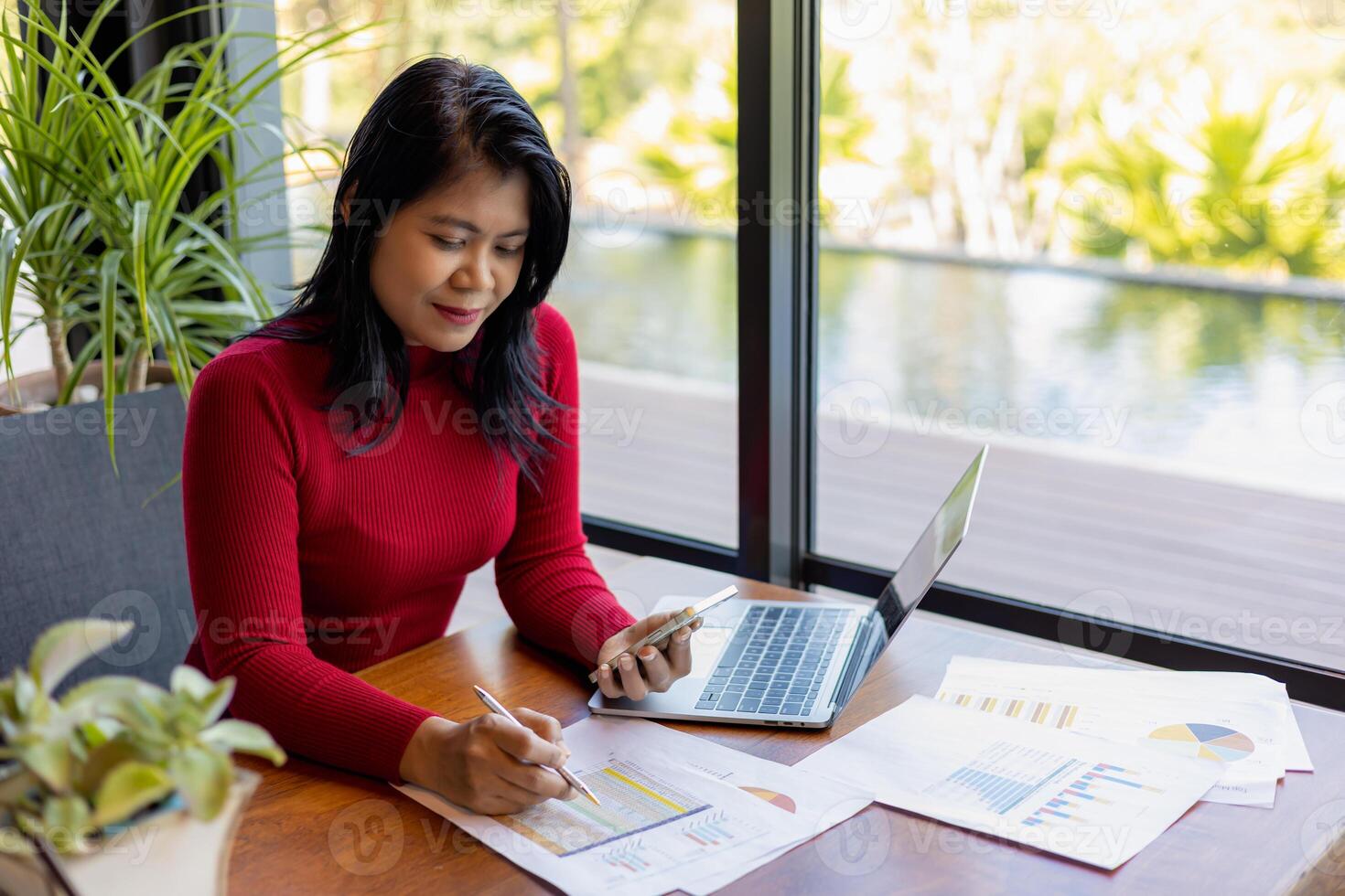 Busness women wearing red sweater working about new startup on smartphone to analysis finance of project in outside office, Woman working using laptop online meeting in home office. photo