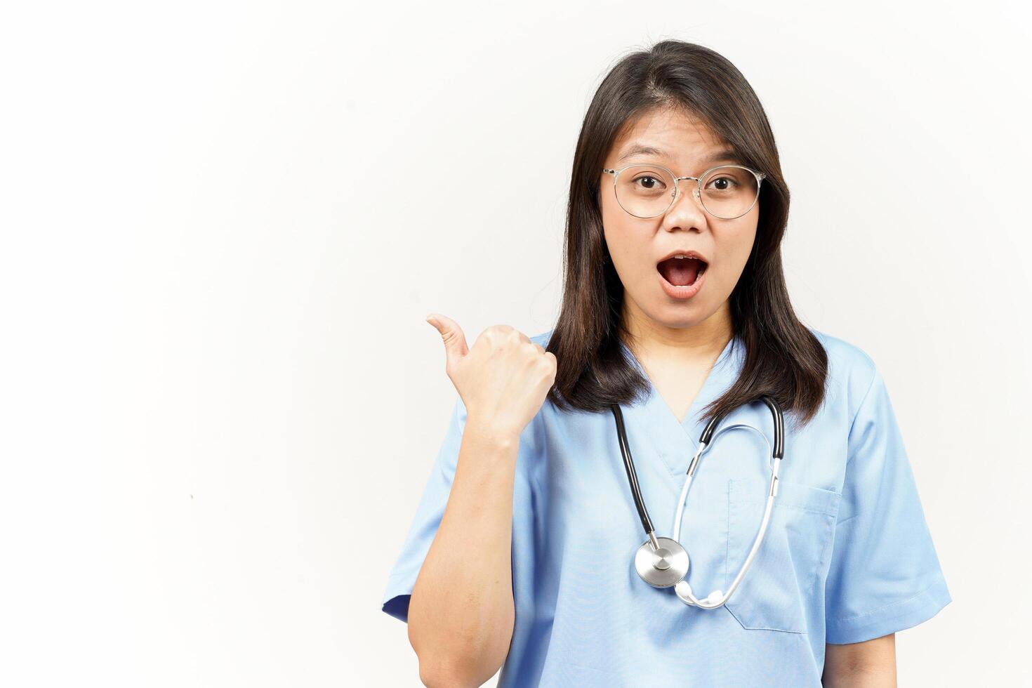 Showing and Pointing Product With Thumb Of Asian Young Doctor Isolated On White Background photo