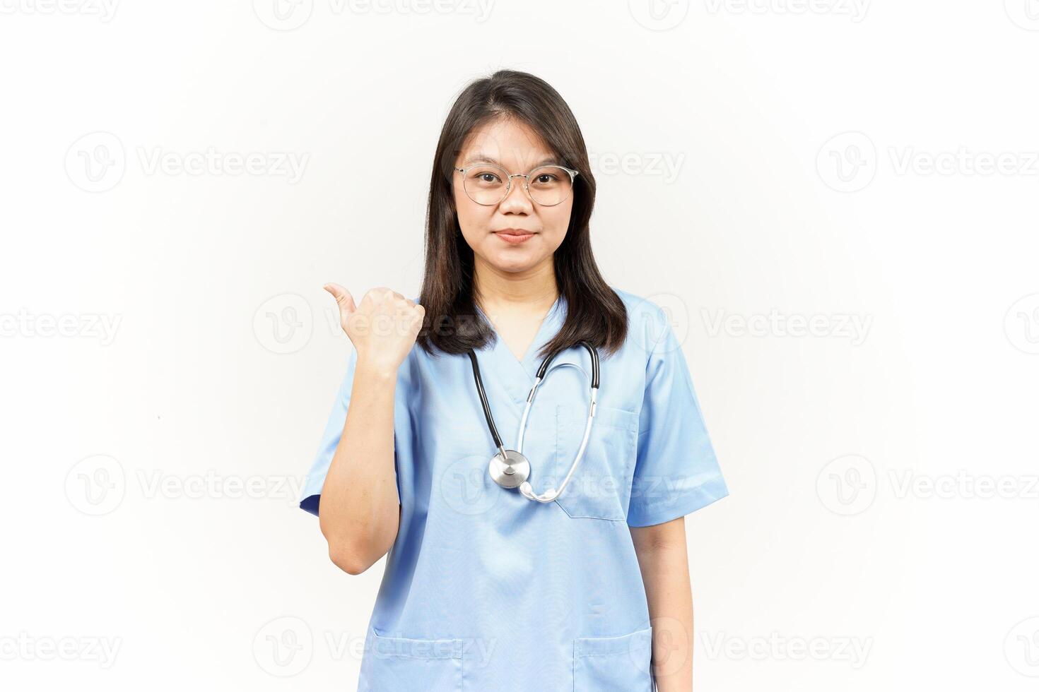 Showing and Pointing Product With Thumb Of Asian Young Doctor Isolated On White Background photo