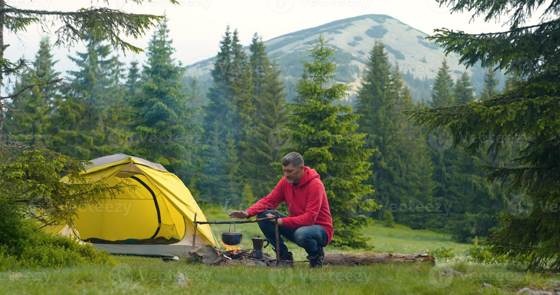 Bearded man near campfire in the forest. The camping is located in a beautiful forest lawn in the mountains. Travel concept photo