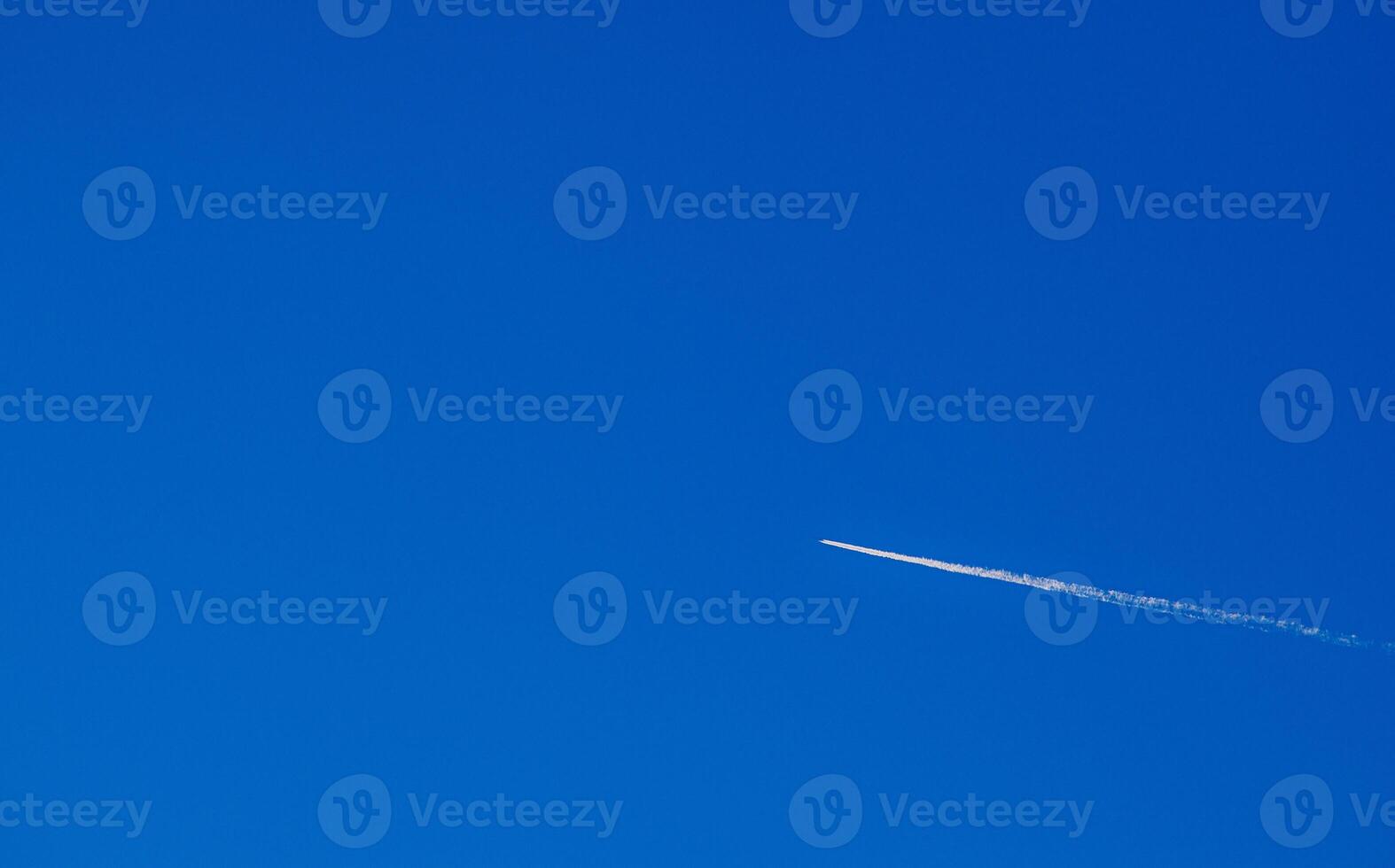 Flight of an airplane with a white trail diagonally against a clear blue sky. For text. photo