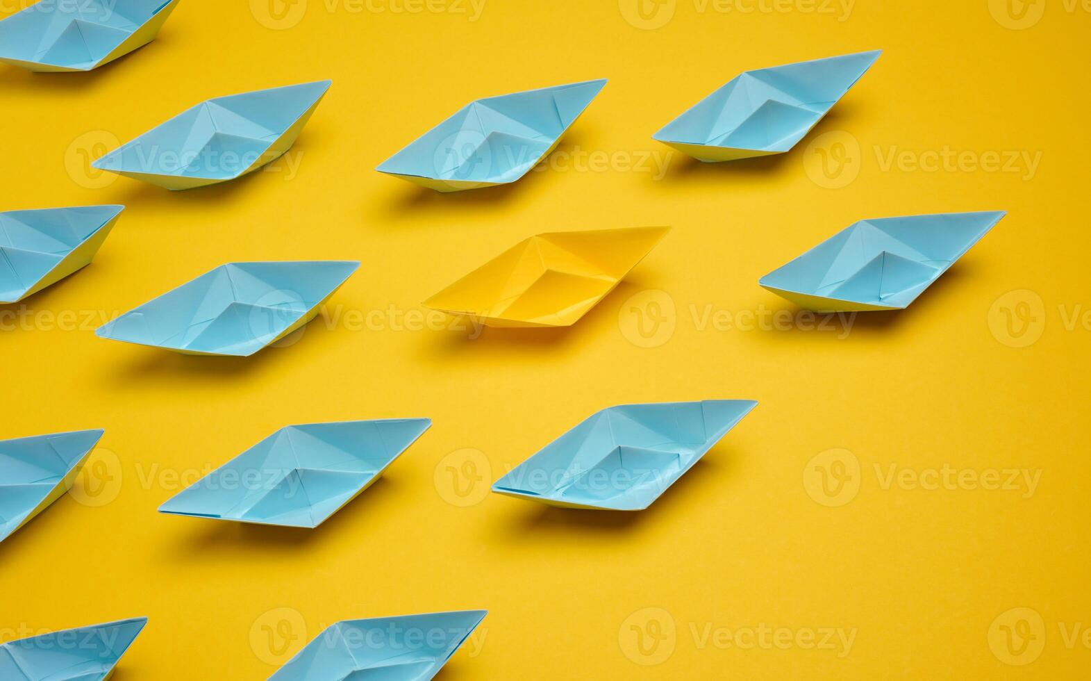 Group of paper boats rushing forward on yellow background, achieving goals photo