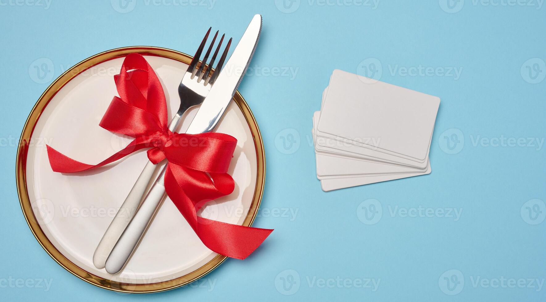 Round white plate and tied with red bow view with knife on blue background photo