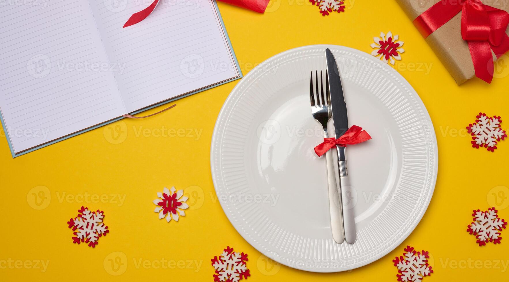 Empty white round plate, fork and knife on yellow background, top view photo
