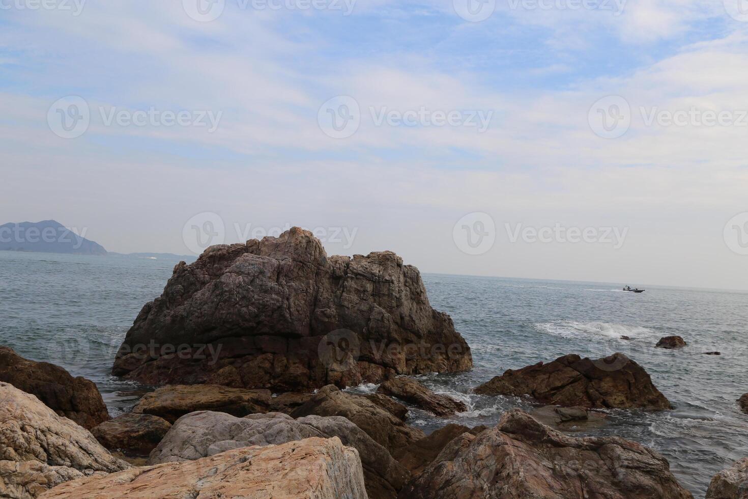 In the sea, there is an island with large rocks on it and boats in front of them photo