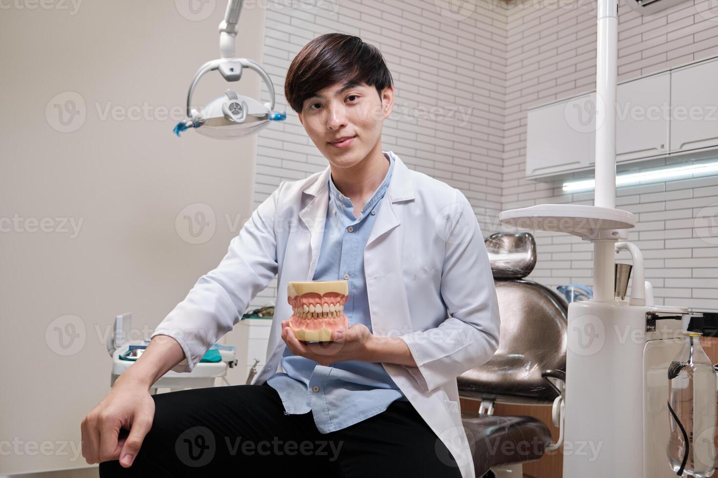 Portrait of one young smart Asian male dentist in uniform, Thai professional dental occupation worker, teeth healthcare, hygiene work in dental clinic hospital, happy smile, and looking at camera. photo