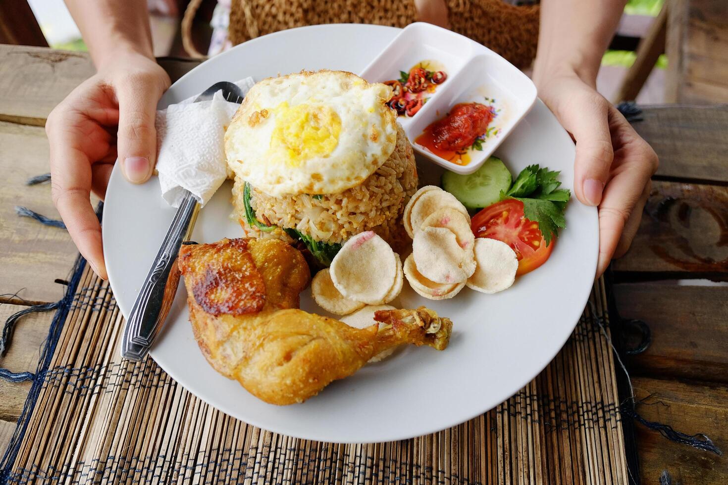 Woman hand holding Pecel ayam or penyet ayam is fried chicken with rice and fried eggs decorated with tomato and spicy sauce is tradition food of Indonesia photo