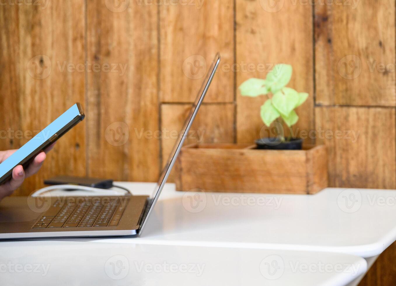 Hand holding smartphone with laptop on desk photo