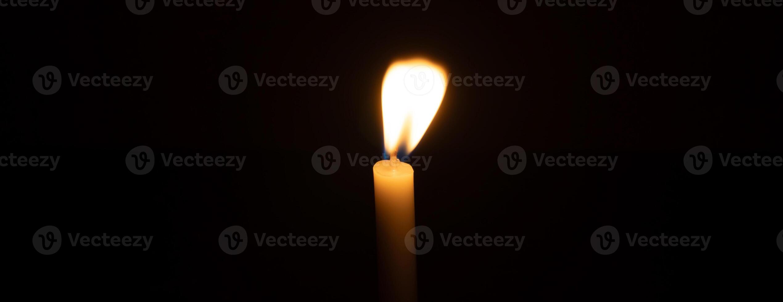A small white candlestick with candlelight for religious ceremony in church is isolated on black background photo