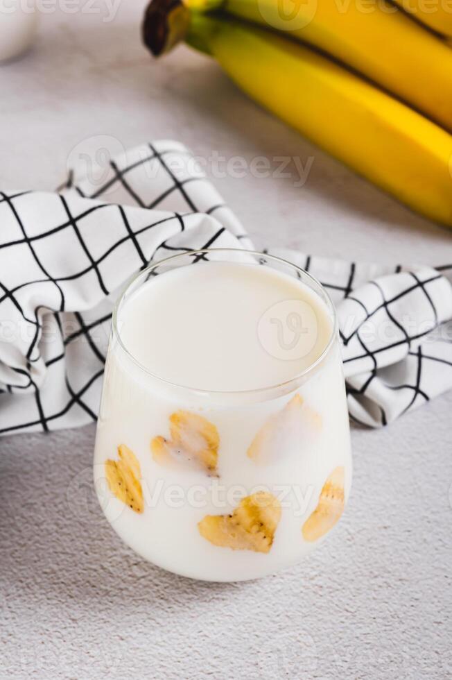 Banana vegan alternative milk in glass and fruits on table vertical view photo