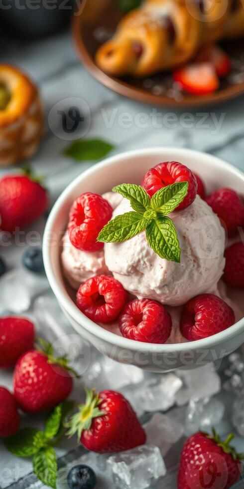 Sweet summer dessert featuring raspberry ice cream in a bowl with fresh berries and mint leaves on a table photo