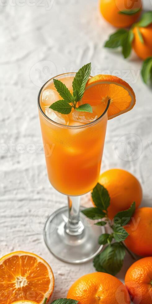 Refreshing orange cocktail garnished with mint on a light background surrounded by fresh oranges photo