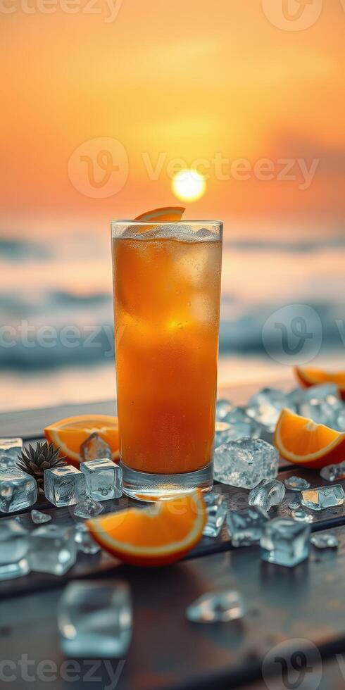 Refreshing cocktail sits on a table with ice and orange slices as the sun sets over the ocean photo