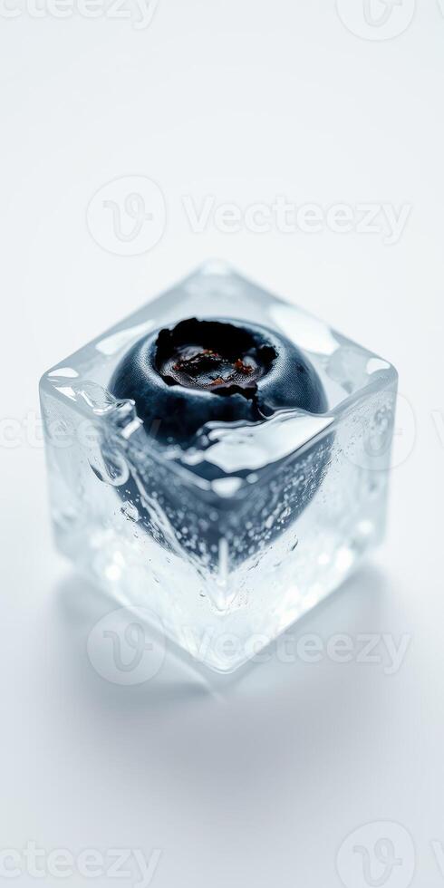 Clear ice cube encasing a single blueberry creates a striking visual on a plain background photo