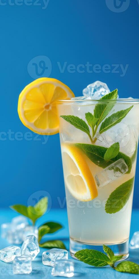 Refreshing lemon mint drink with ice served in a clear glass against a vibrant blue background photo
