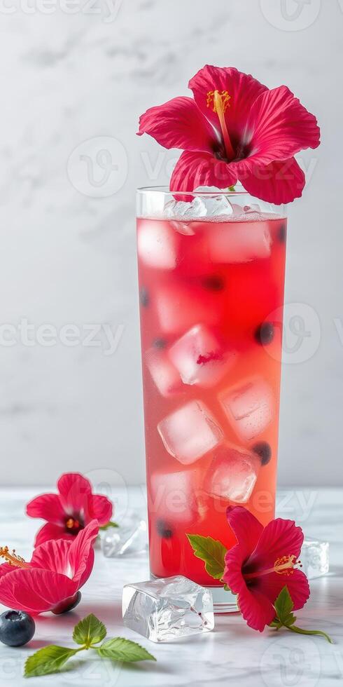 Refreshing hibiscus drink served in a tall glass with ice, garnished with vibrant flowers on a marble surface photo