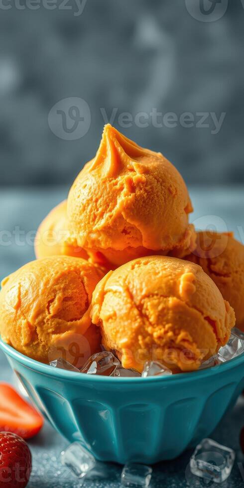 Delicious orange ice cream scoops served in a blue bowl with fresh strawberries on a cool stone surface photo