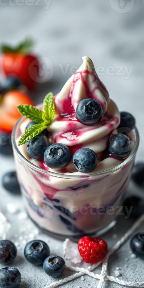 Creamy dessert with fresh blueberries and strawberries served in a glass cup, topped with syrup and mint leaf photo