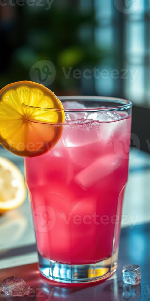 Refreshing pink drink with ice and lemon slice served in a clear glass during sunny afternoon indoors photo