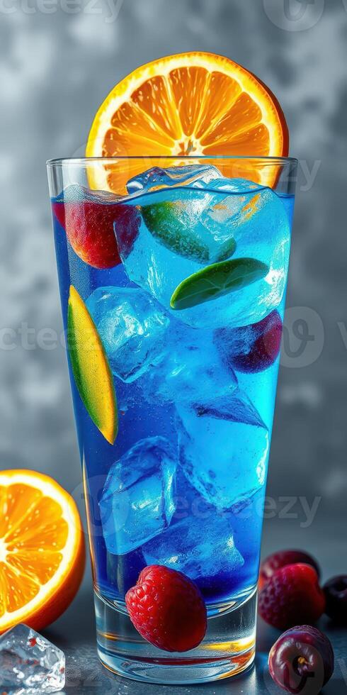Refreshing blue beverage served in a tall glass garnished with orange slices and mixed berries on a gray background photo