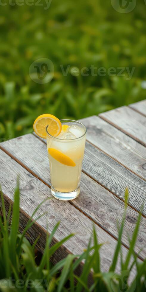 Refreshing lemonade served in a glass with lemon slices on a wooden table surrounded by green grass photo